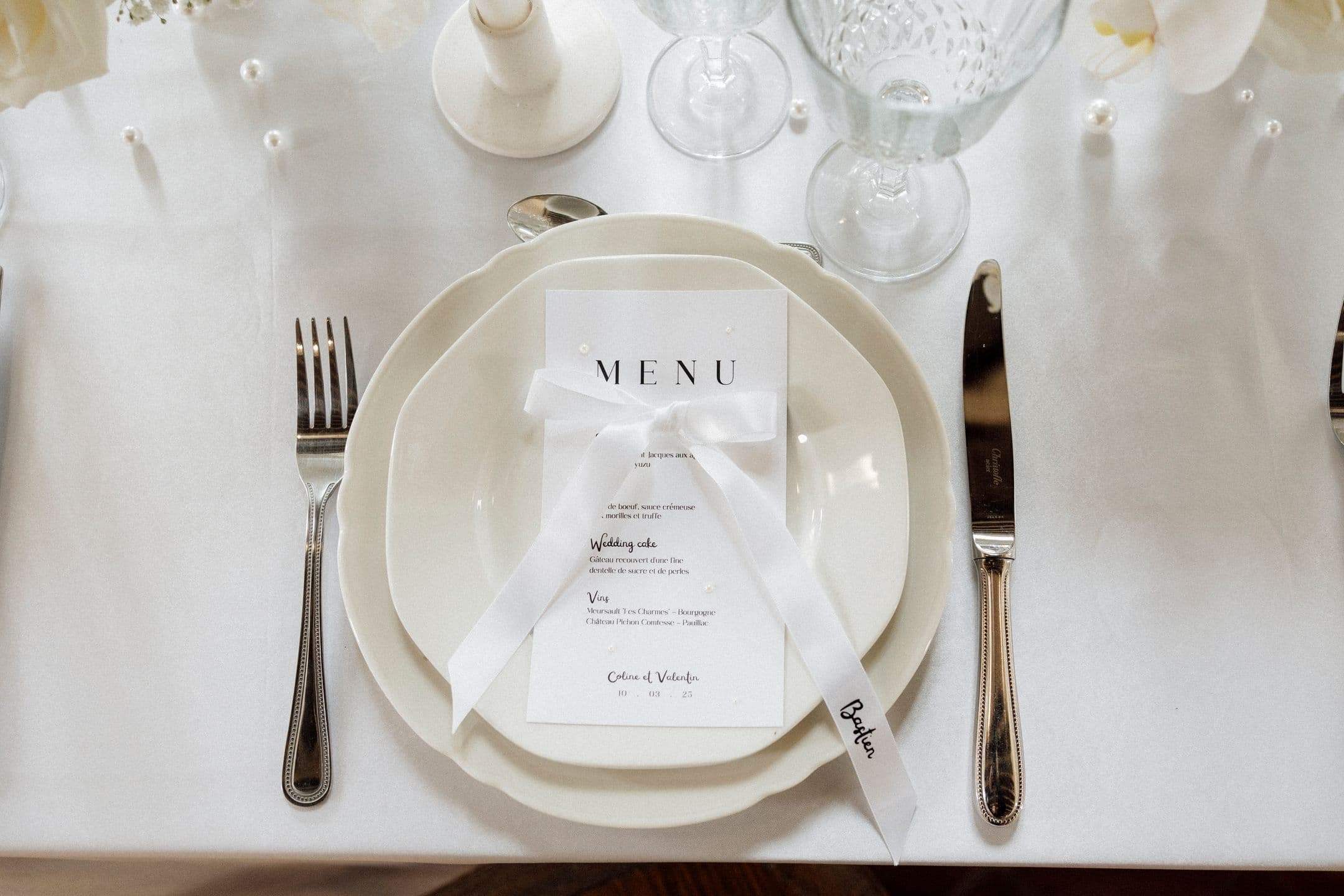Assiette avec menu noué d'un ruban blanc et perles éparpillées sur la nappe