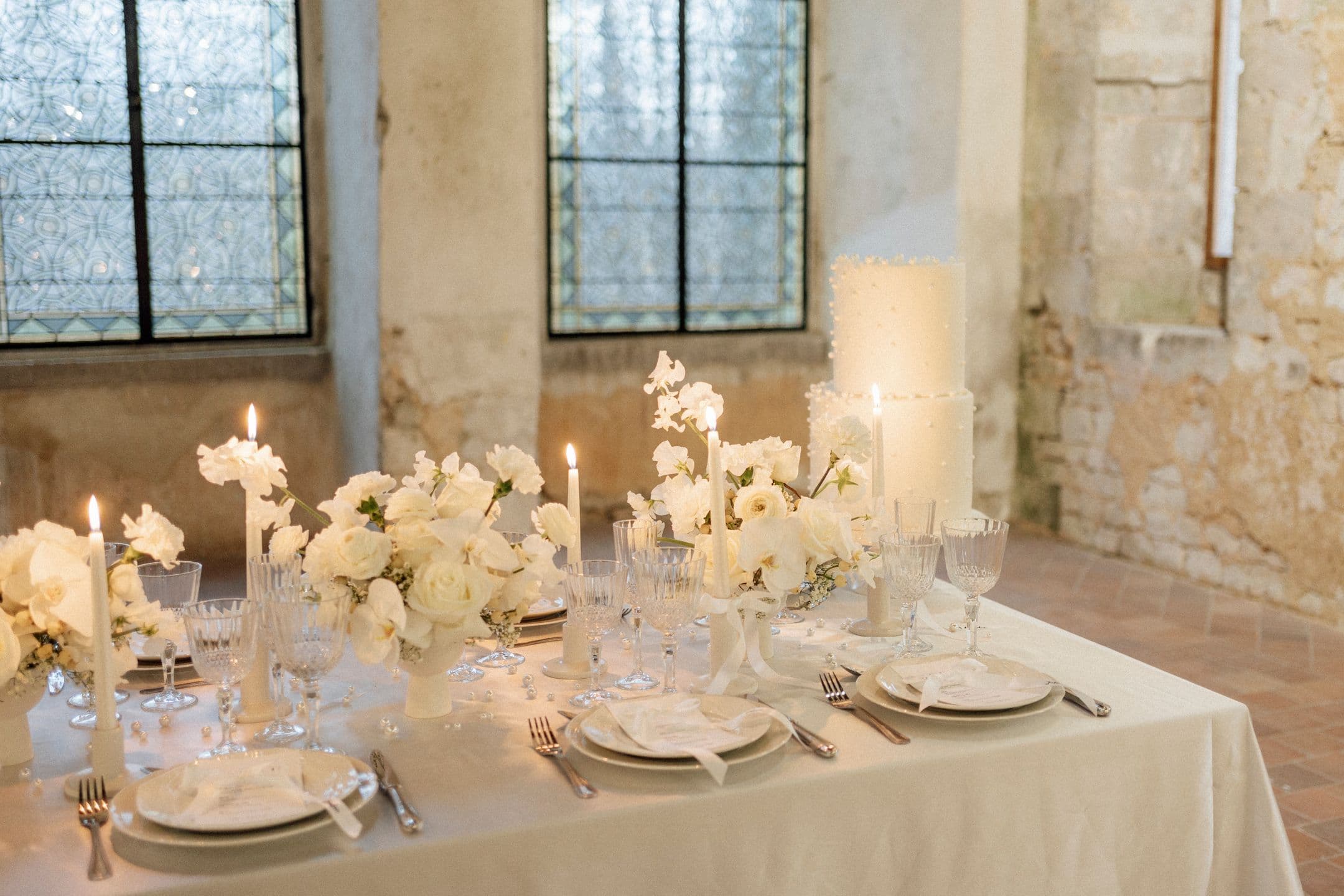 Table de mariage aux chandelles et fleurs blanches devant des vitraux
