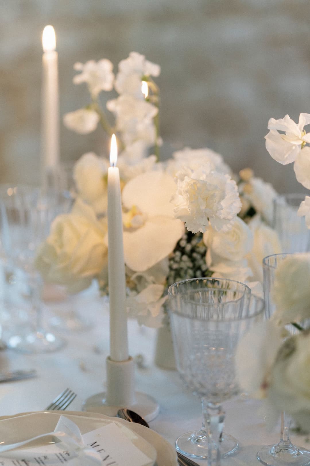 Chandelles, fleurs blanches et verres ciselés sur une table de mariage
